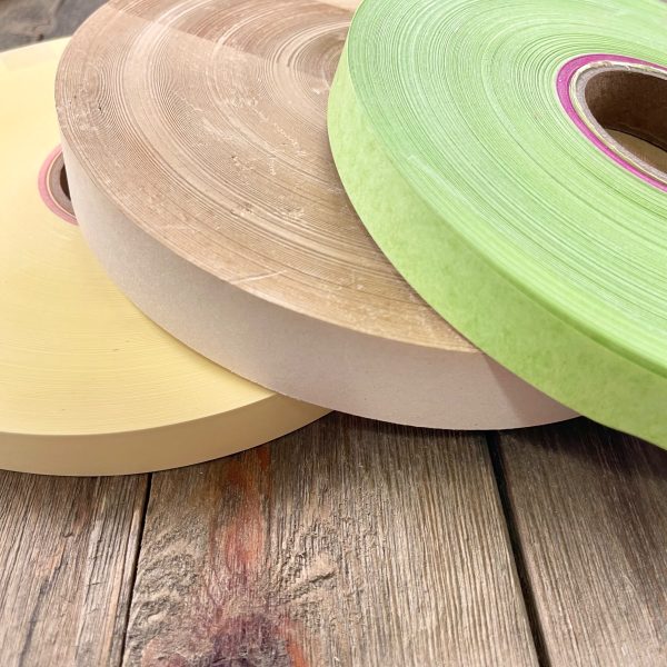Three large rolls of vintage teletype tape in yellow, beige, and lime green