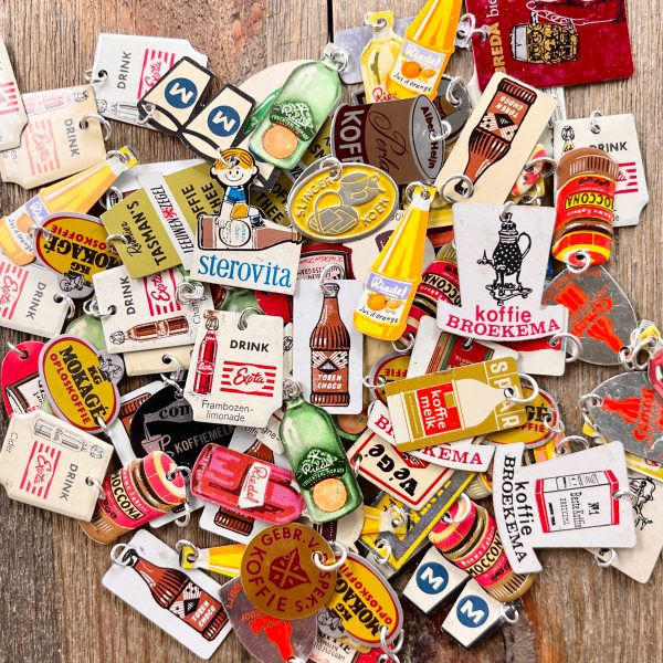 A large pile of colorful vintage drink-themed Dutch advertising pins-turned-charms with silver jump rings