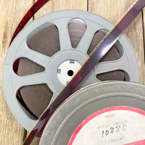 A vintage metal film reel and case with the 16mm film strip showing on top of the reel