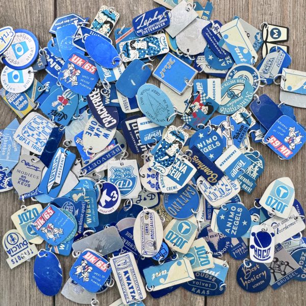 A pile of blue handmade journal charms made from vintage metal Dutch advertising stick pins